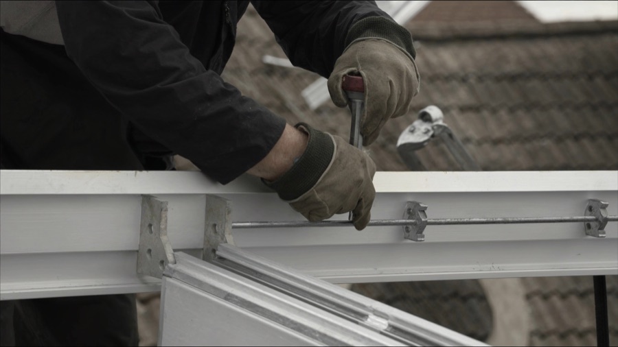 Monteurshände in Arbeitshandschuhen ziehen eine Schraube an der Aluminium-Unterkonstruktion fest